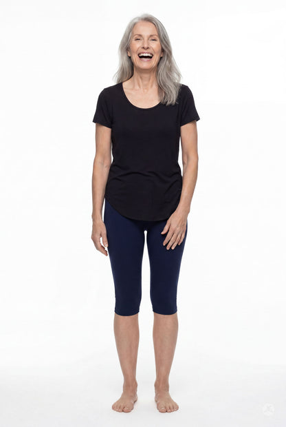 Smiling woman wearing SweetLegs Knee-Length Capri in navy blue paired with black top standing barefoot on white background