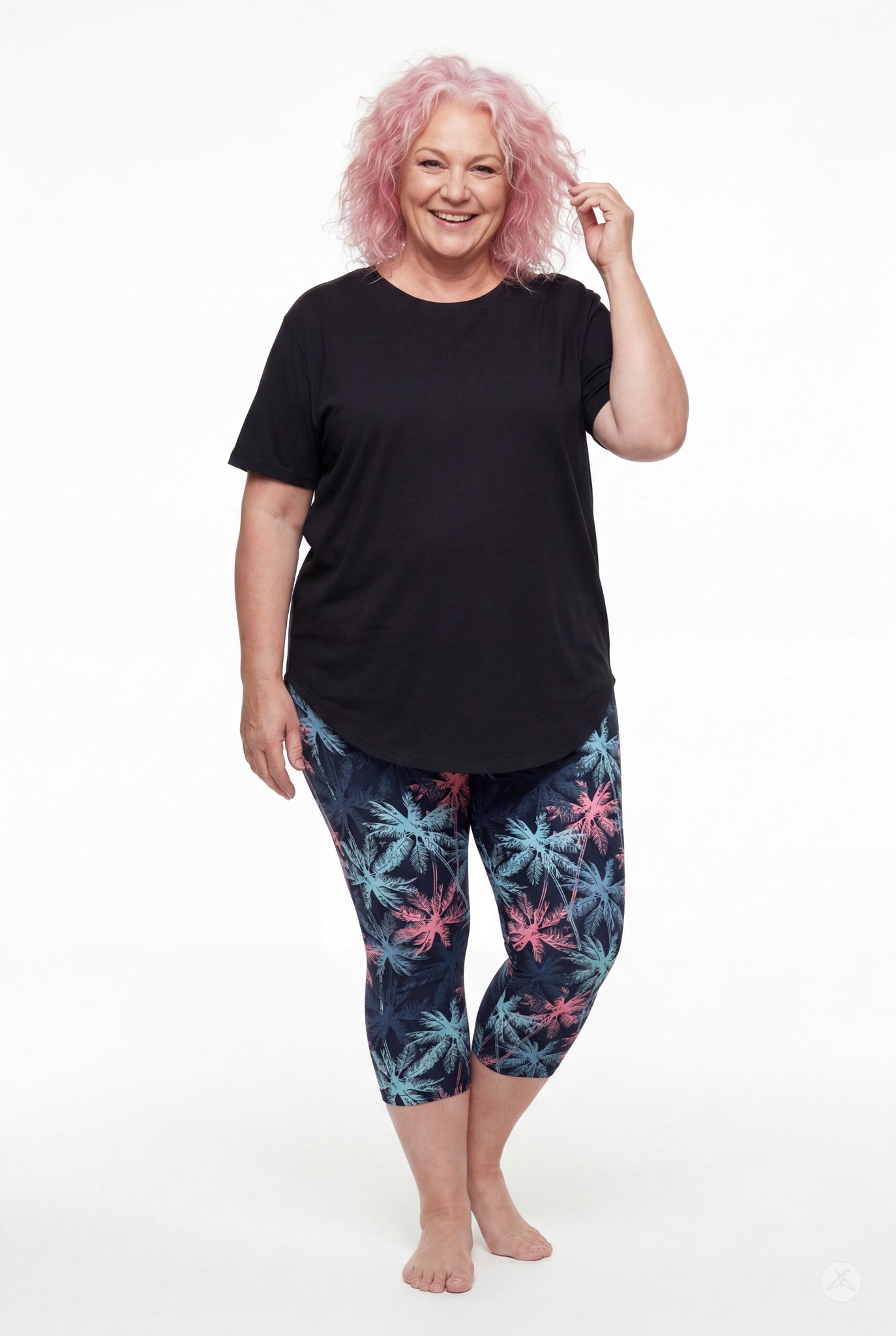 Smiling woman wearing SweetLegs Tiki Nights Crops with pink and blue palm pattern and black short sleeve top barefoot