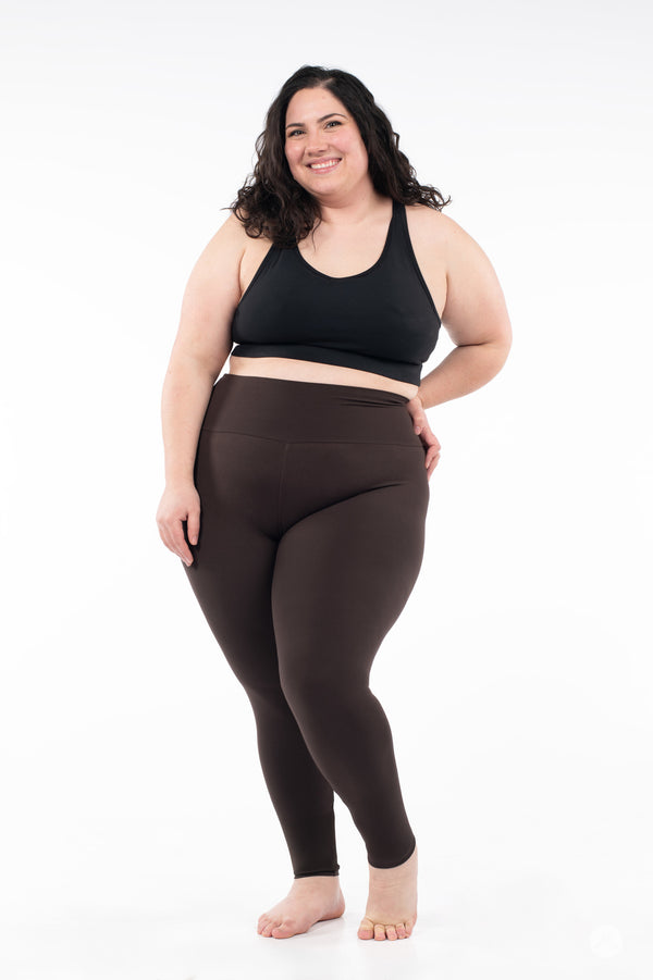Plus size model smiling and wearing SweetLegs Espresso High-Waisted Leggings in brown with a black tank on white background