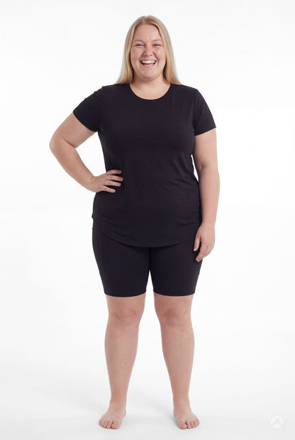 Smiling plus size woman wearing SweetLegs Black Pocket Biker Shorts with black tee standing front view barefoot