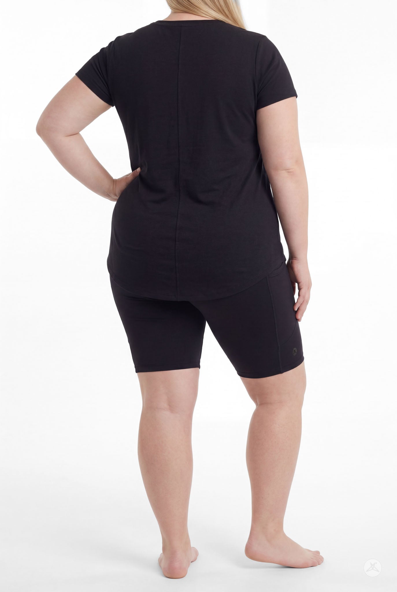 Plus size woman standing barefoot wearing SweetLegs Black Pocket Biker Shorts with a black short sleeve top rear view