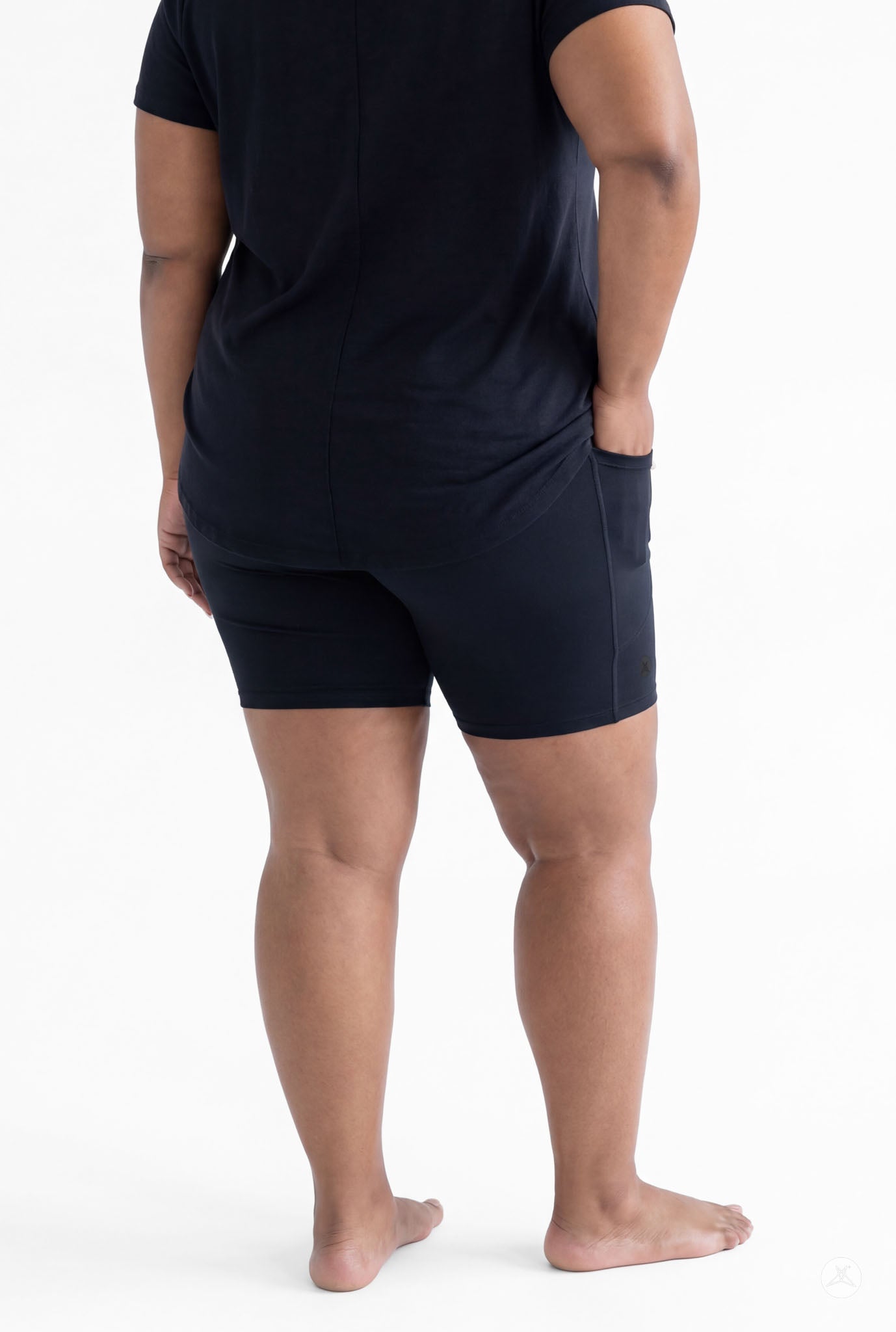Plus size woman standing barefoot wearing SweetLegs Black Pocket Biker Shorts and black top rear view with hands relaxed