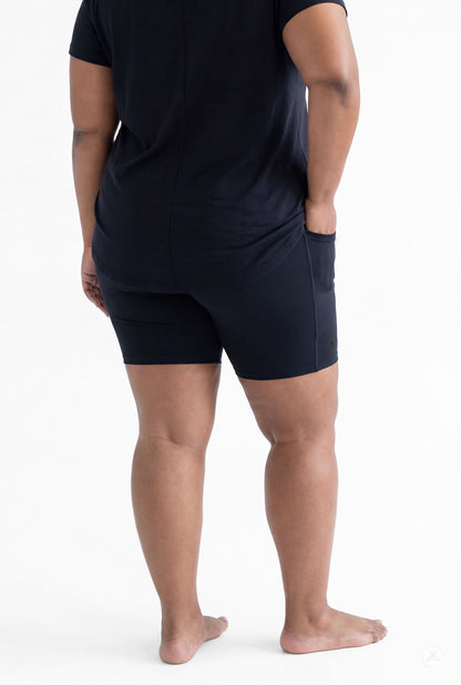 Plus size woman standing barefoot wearing SweetLegs Black Pocket Biker Shorts and black top rear view with hands relaxed