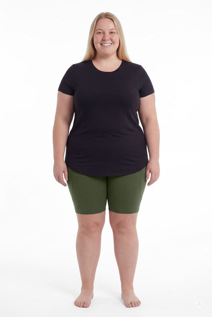 Smiling woman wearing SweetLegs Cedar Pocket Biker Shorts in green and black top standing barefoot front view