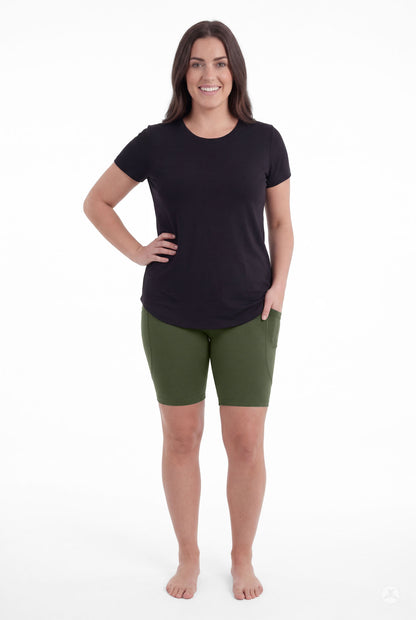 Woman smiling barefoot wearing SweetLegs Cedar Pocket Biker Shorts in green with hand in side pocket standing front view
