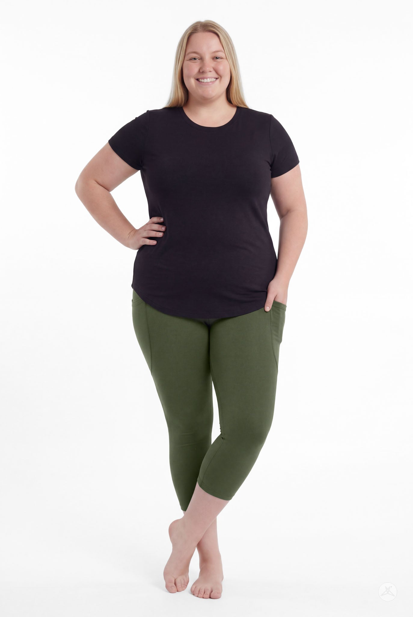 Plus size woman standing barefoot wearing SweetLegs Cedar Pocket Crops in green with black short sleeve top and hand in pocket
