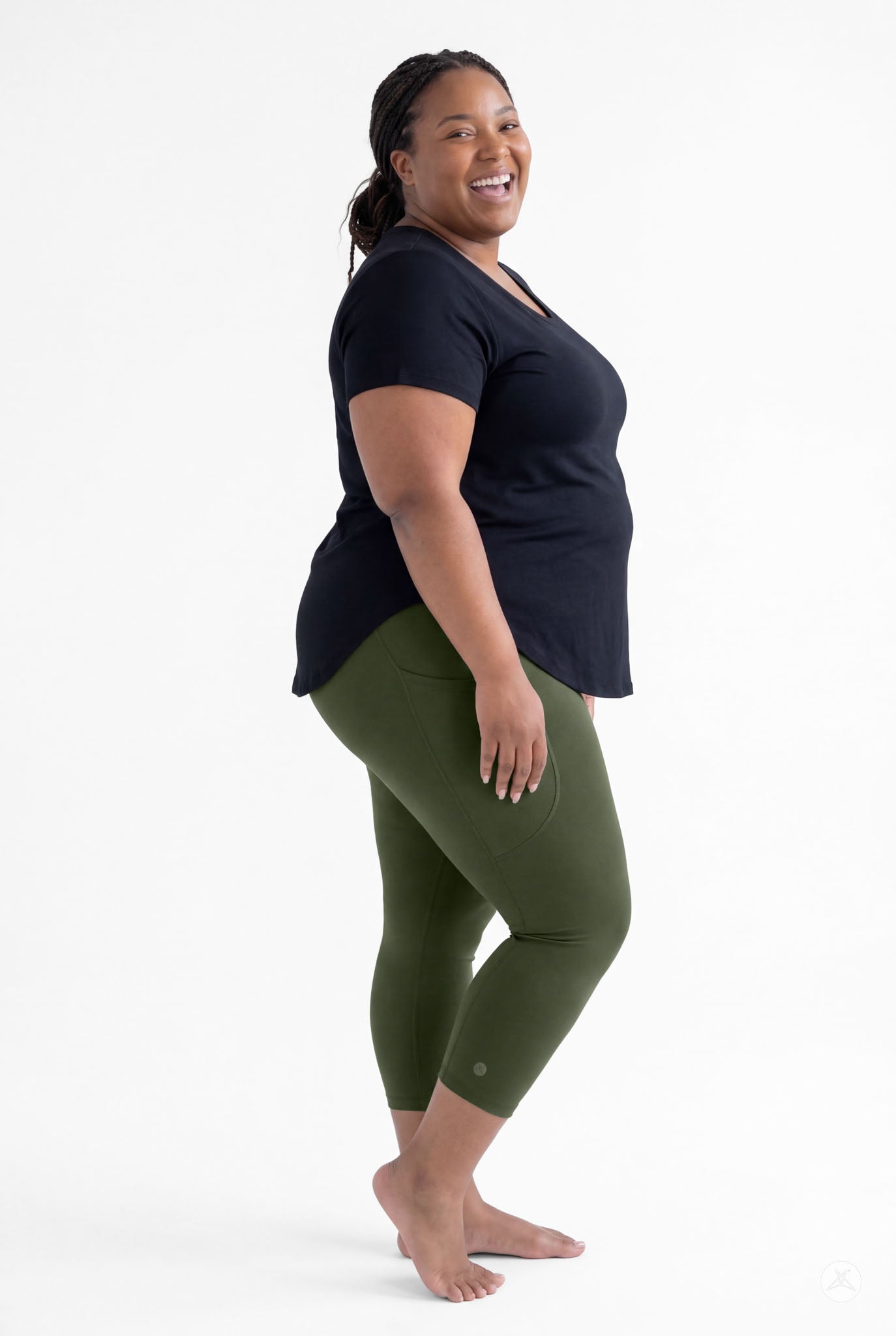 Plus size woman smiling wearing SweetLegs Cedar Pocket Crops in olive green leggings and black short sleeve top barefoot