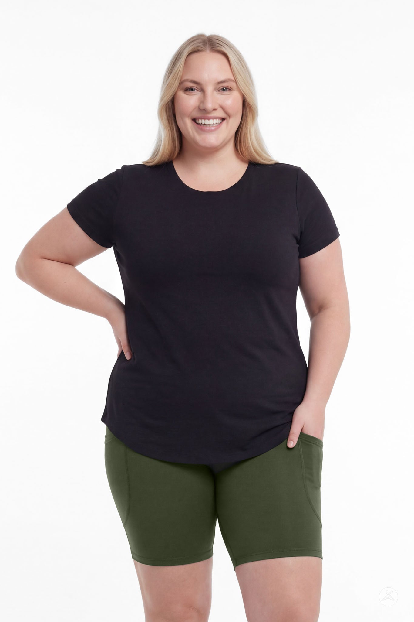 Smiling woman in black top wearing SweetLegs Cedar Pocket Biker Shorts in green with hand in pocket front view