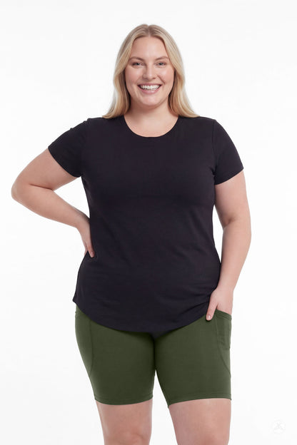 Smiling woman in black top wearing SweetLegs Cedar Pocket Biker Shorts in green with hand in pocket front view