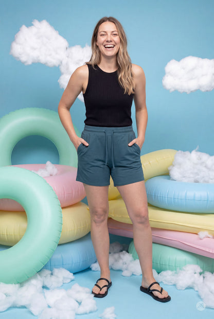 Smiling woman wearing teal Lounge Shorts by SweetLegs with pockets and drawstring waist against playful pastel background
