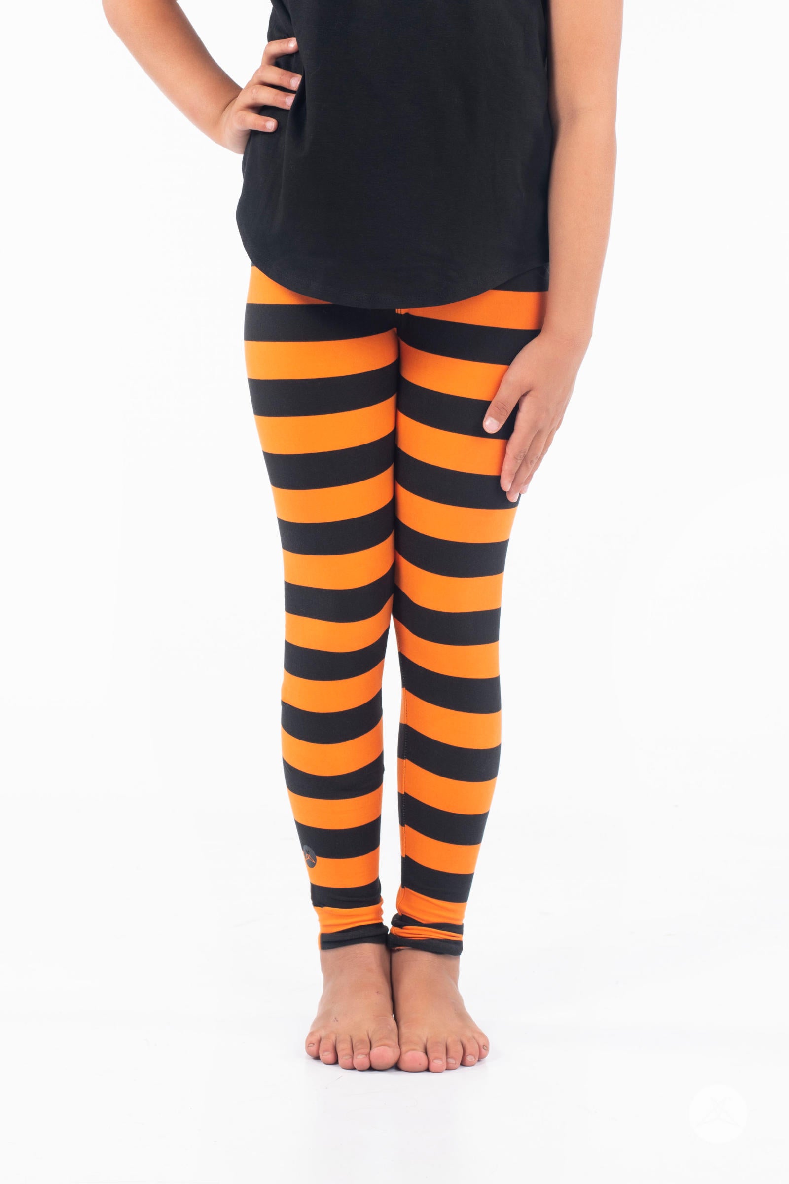 Cauldron Bubbles Kids leggings by SweetLegs featuring bold black and orange wide horizontal stripes on child model barefoot